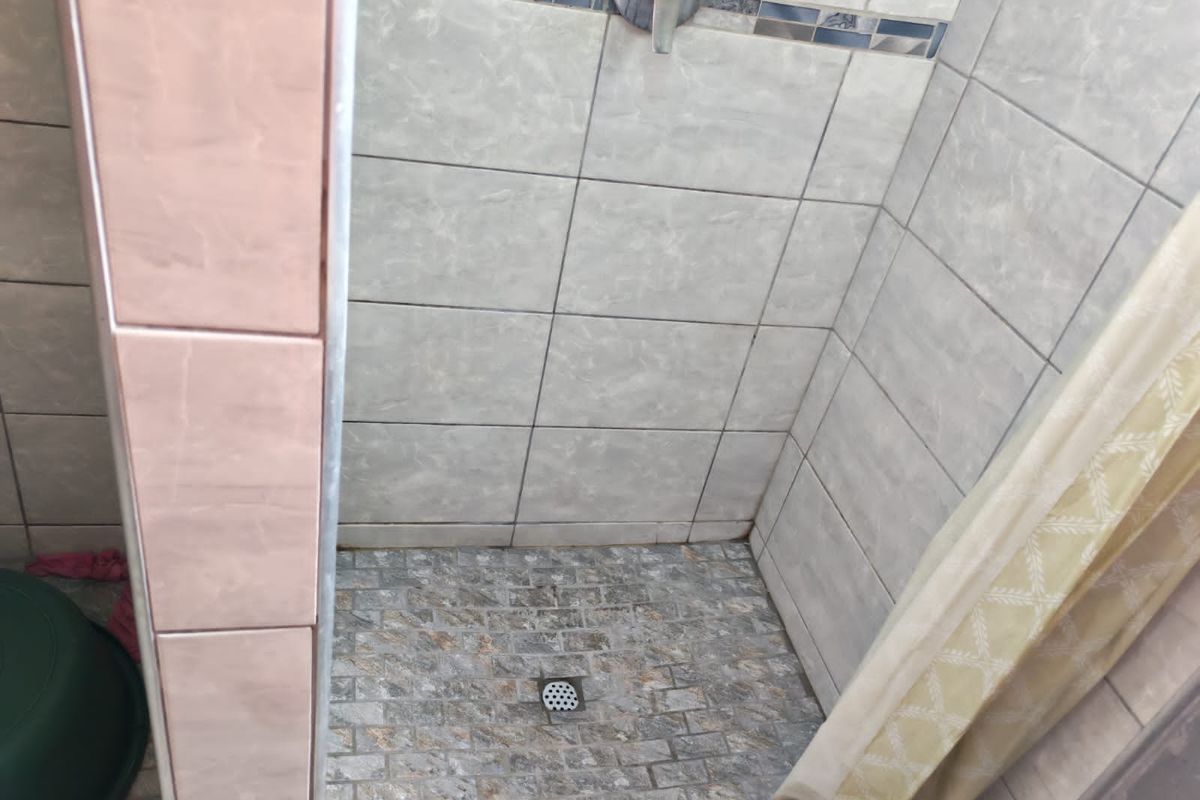 A functional shower enclosure featuring tiled walls with a decorative border and a textured stone-look floor tile.