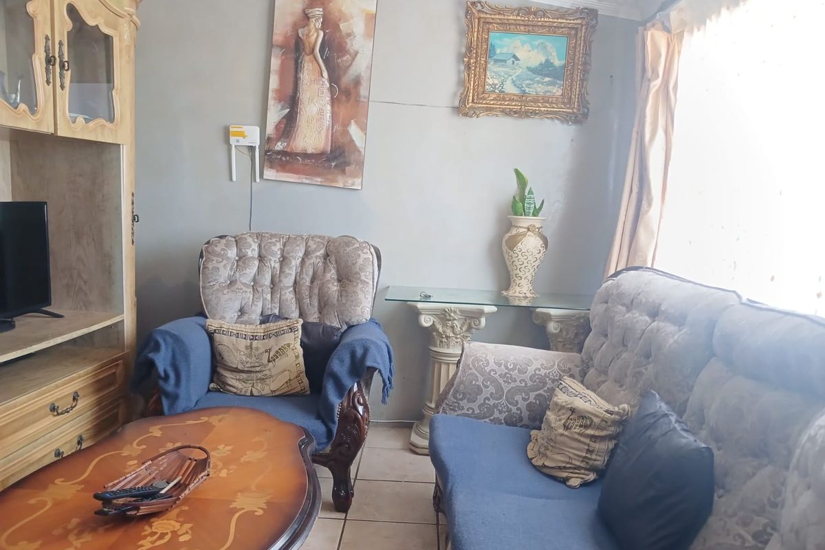 A living room area featuring tiled flooring and decorative ceiling cornicing, currently showing signs of wear on the wall surfaces.