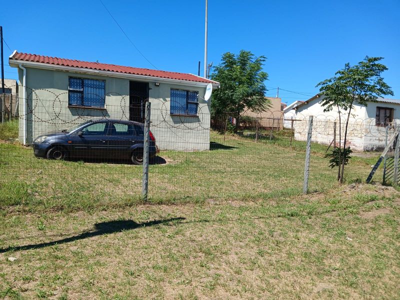 Front view of a detached house featuring security fencing, razor wire, and security bars on windows, set on a grassed plot.