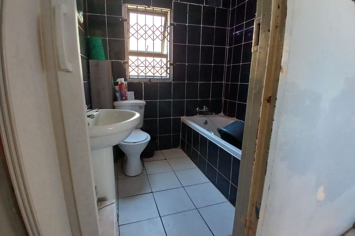 A dated bathroom featuring black wall tiles, a white pedestal basin, toilet, and bathtub, requiring cosmetic updates to improve its overall condition.