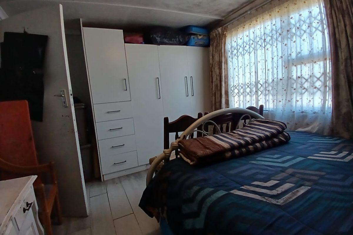 A bedroom featuring built-in wardrobes and a window with a security gate, showing signs of wear on the ceiling and flooring.