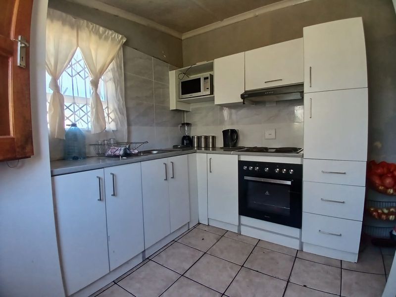 Compact kitchen featuring white built-in cabinetry, integrated oven and hob, tiled backsplash, and tiled flooring.