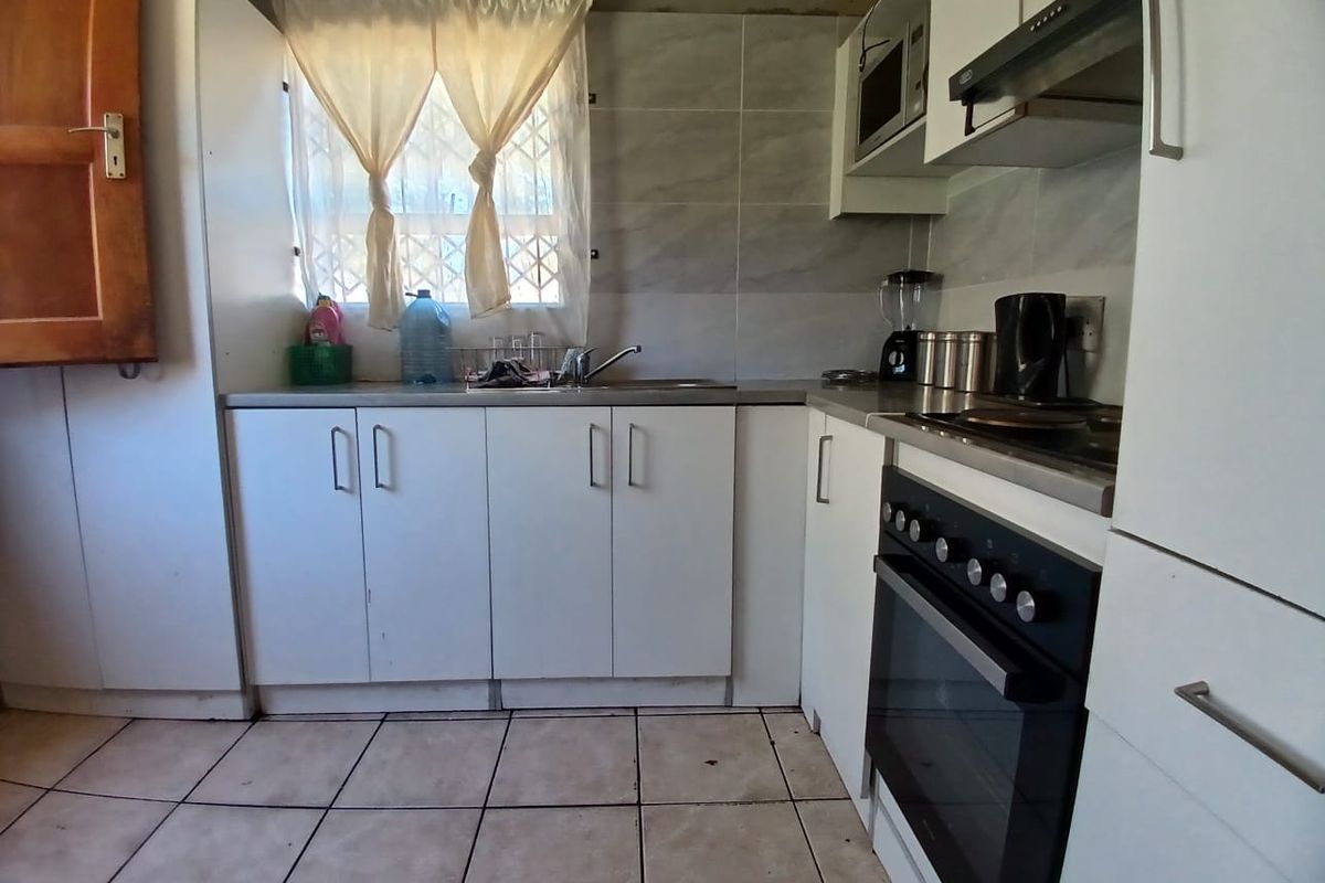 Compact kitchen featuring white cabinetry, built-in oven with hob, extractor fan, and tiled splashback. Requires cosmetic updates to ceiling and flooring.