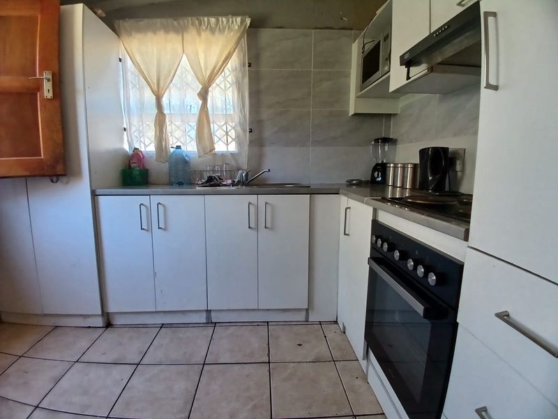 Compact kitchen featuring white cabinetry, built-in oven with hob, extractor fan, and tiled splashback. Requires cosmetic updates to ceiling and flooring.