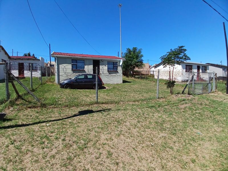 Front view of a detached house featuring a fenced yard, security bars on windows, and a corrugated metal roof.