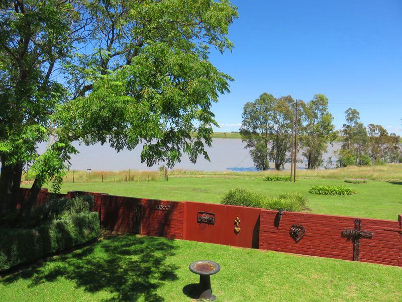 A scenic view of the garden and lawn area overlooking a large dam or lake, featuring a decorative brick boundary wall.