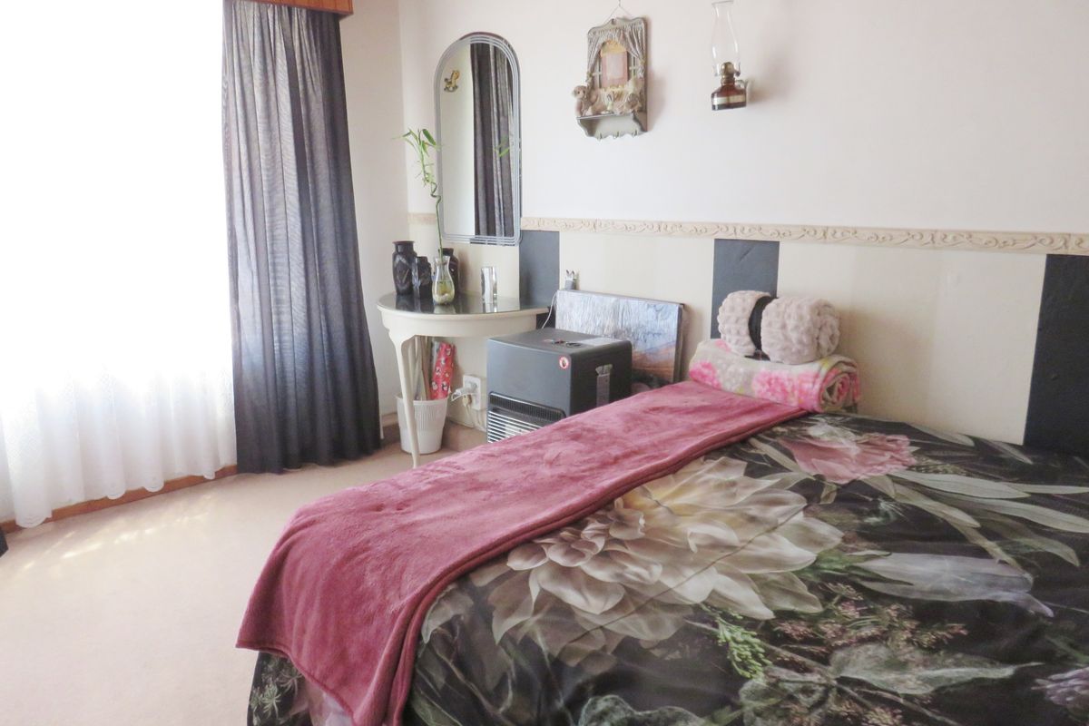 A bedroom featuring neutral walls, carpeted flooring, and a large window with curtains, providing a functional and lived-in space.