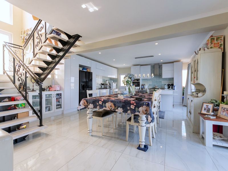 Spacious open-plan living and dining area featuring modern glossy kitchen cabinetry, sleek tiled flooring, and a striking feature staircase with wrought iron detailing.