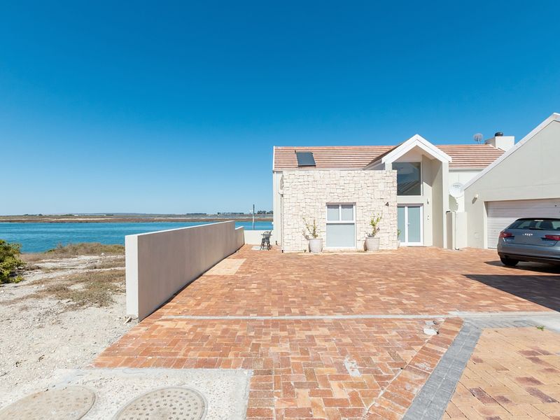 Front exterior view of a modern house featuring stone cladding, a brick-paved driveway, double garage, and scenic waterfront views.