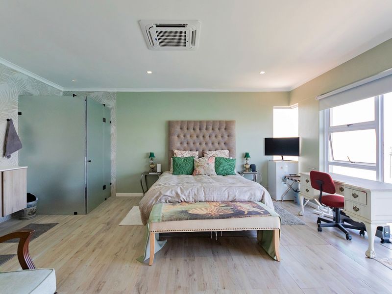 Spacious bedroom featuring light laminate flooring, a ceiling-mounted air conditioning unit, and a modern frosted glass partition enclosing an en-suite vanity area.