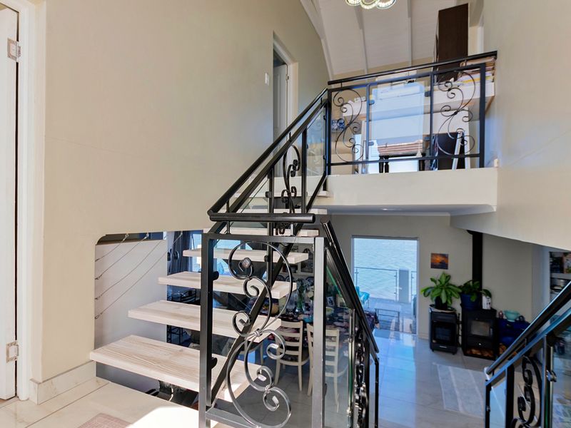 A bright, open-plan hallway featuring a modern open-tread staircase with decorative wrought iron railings, leading to a mezzanine level with vaulted ceilings.