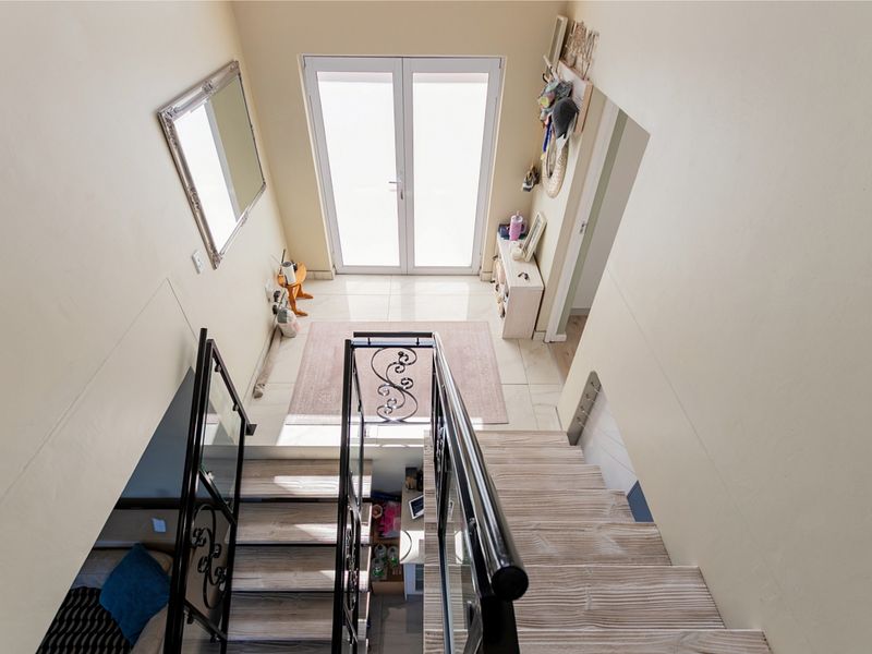 A bright entrance foyer featuring a staircase with a decorative wrought iron balustrade and tiled flooring, leading to double glass entrance doors.