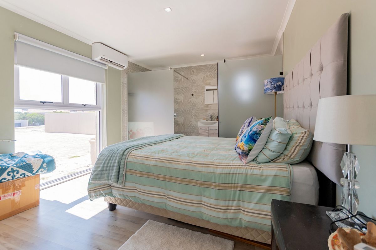 A well-lit bedroom featuring laminate flooring, a split-system air conditioner, and an integrated en-suite bathroom with a frosted glass partition.