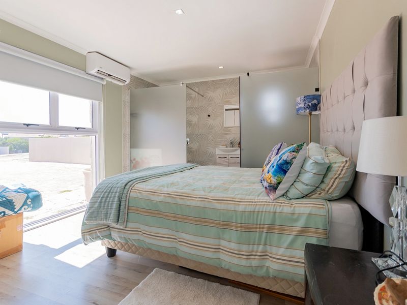 A well-lit bedroom featuring laminate flooring, a split-system air conditioner, and an integrated en-suite bathroom with a frosted glass partition.