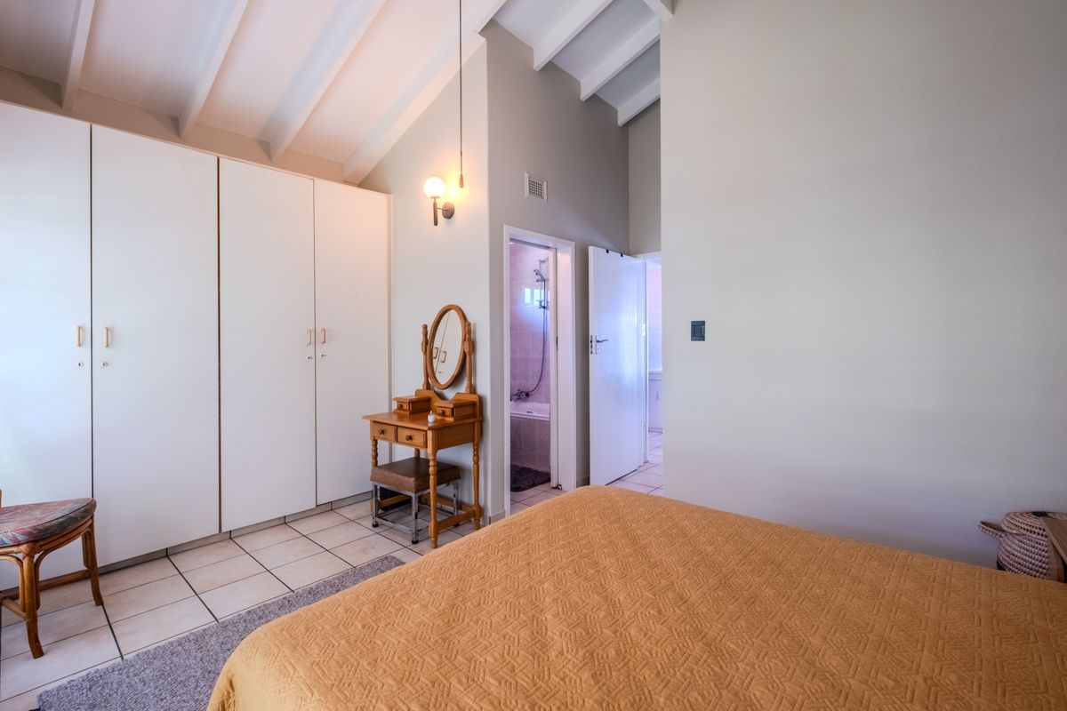 A bedroom featuring vaulted ceilings with exposed rafters, built-in cupboards, tiled flooring, and direct access to an en-suite bathroom.