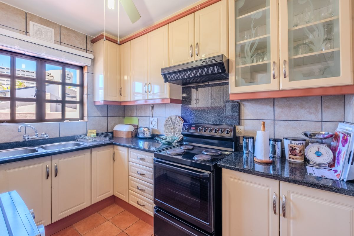 A functional kitchen featuring granite countertops, ample built-in cabinetry, a tiled backsplash, and a freestanding stove with an extractor fan.