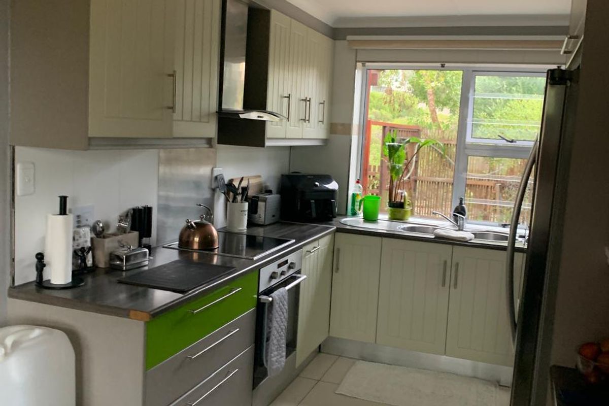 A functional kitchen featuring built-in cabinetry, a stainless steel sink, an electric hob with an extractor fan, and tiled flooring with natural light.