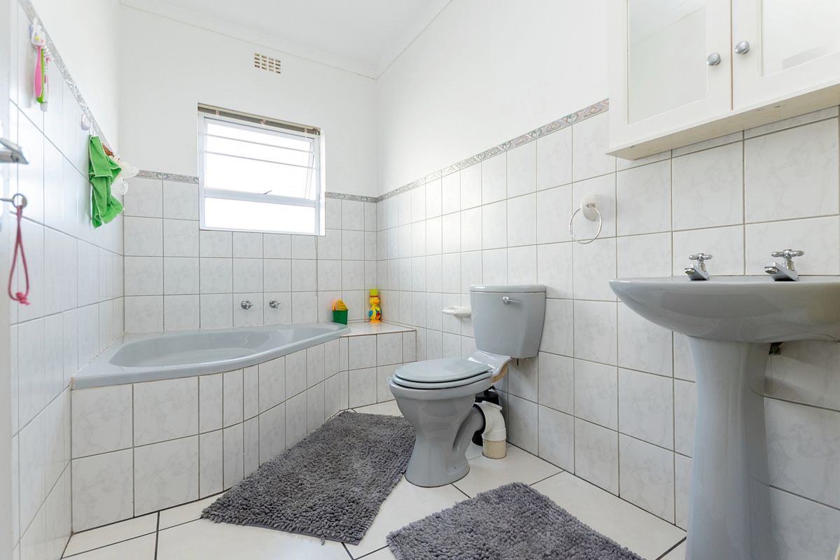 A functional bathroom featuring a built-in bathtub, pedestal basin, and toilet, finished with neutral wall and floor tiling.