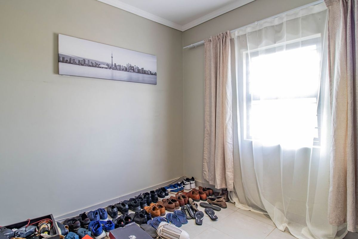 A neutral bedroom space featuring tiled flooring and natural light through a window with installed curtain rails.