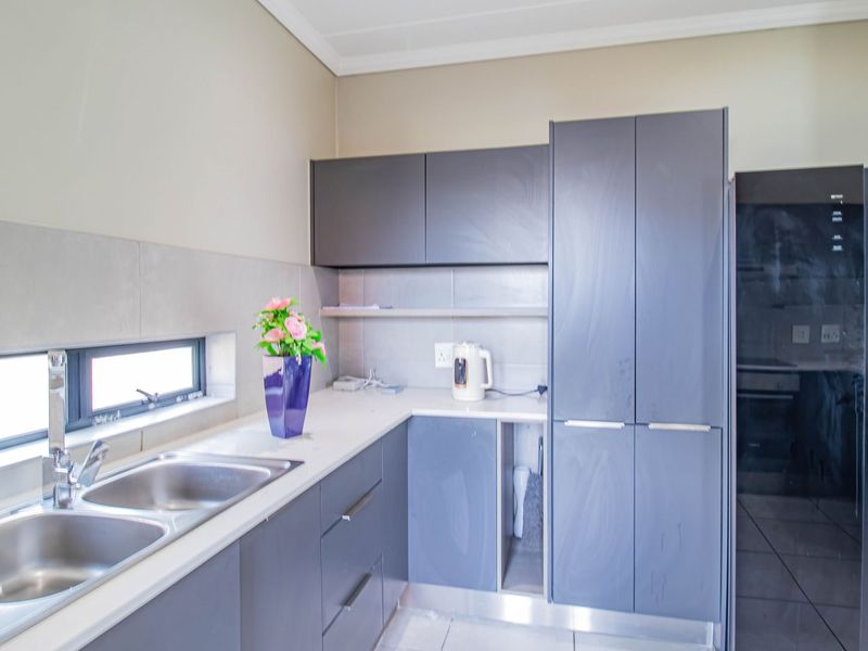 Kitchen featuring grey cabinetry, stone countertops, a double bowl stainless steel sink, and tiled backsplash. Note the missing cabinet door under the counter.