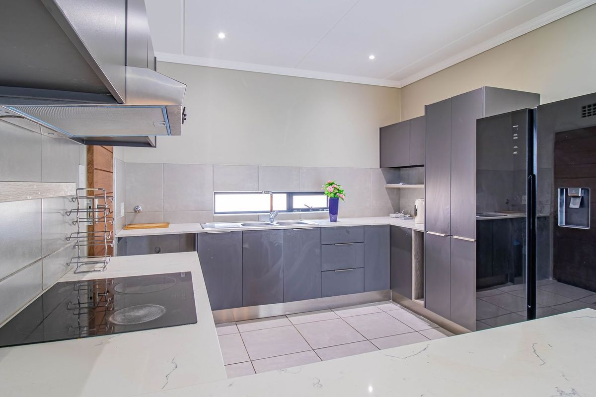 Modern kitchen featuring sleek dark grey cabinetry, stone countertops, integrated electric hob, extractor fan, and tiled flooring with recessed lighting.