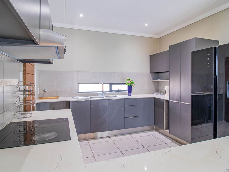 Modern kitchen featuring sleek dark grey cabinetry, stone countertops, integrated electric hob, extractor fan, and tiled flooring with recessed lighting.