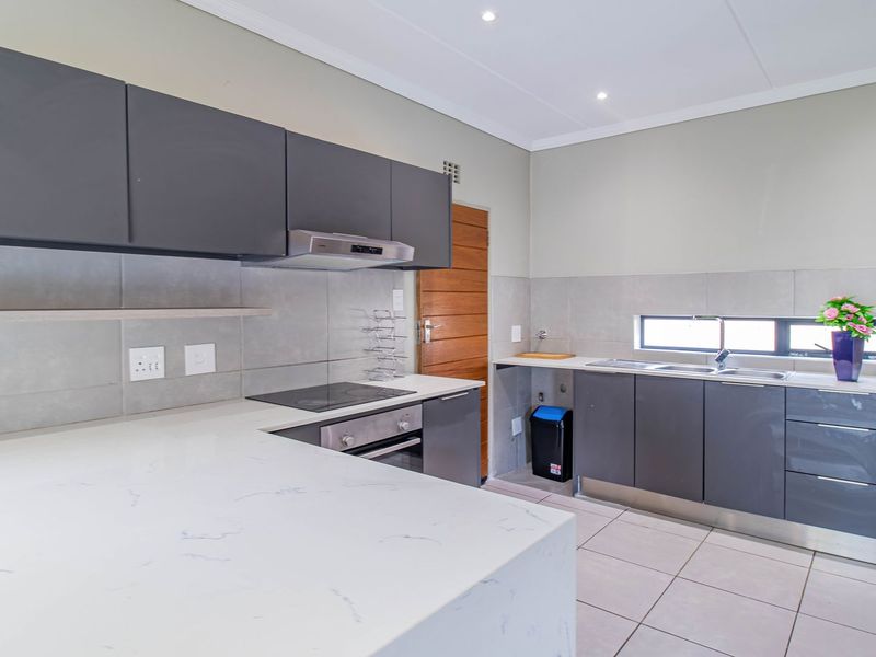 Modern kitchen featuring dark grey cabinetry, stone countertops, integrated electric hob and oven, and tiled flooring with recessed lighting.