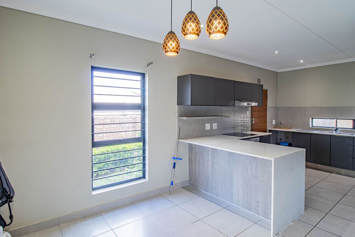 Modern kitchen featuring dark cabinetry, stone countertops, an electric hob with extractor, and tiled flooring, offering a clean and functional workspace.