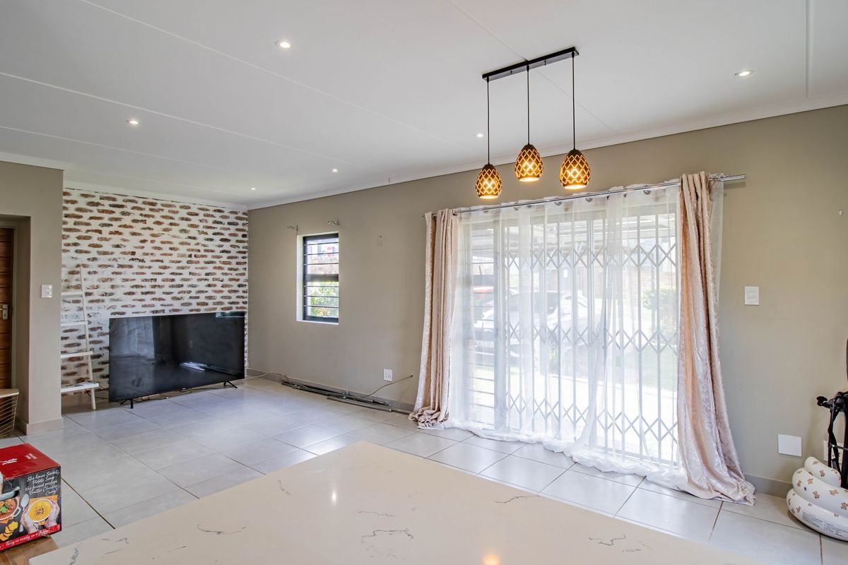 Spacious living area featuring a decorative exposed brick wall, tiled flooring, modern pendant lighting, and a sliding door providing access to the exterior.