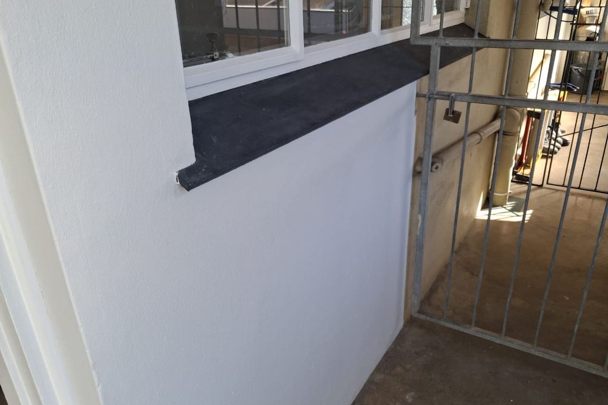 A view of an exterior wall section featuring a window with a dark sill and a metal security gate.