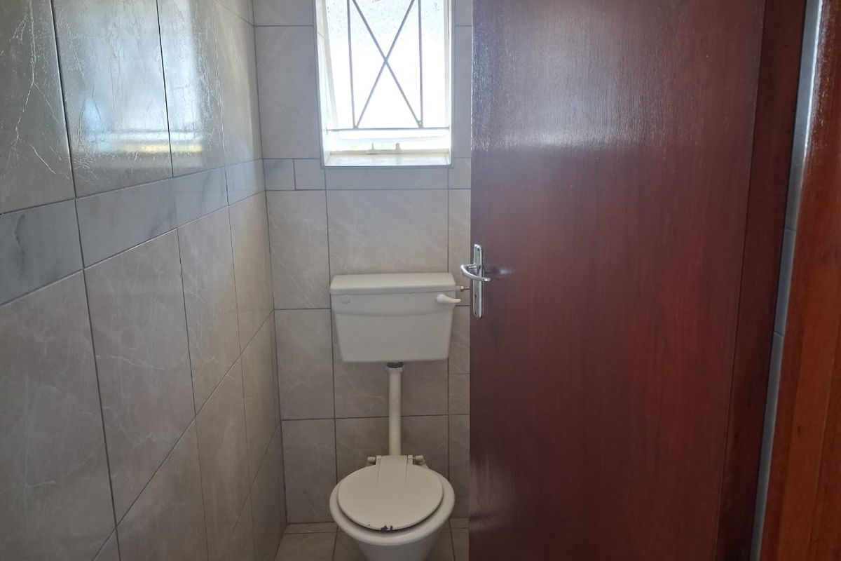A compact bathroom featuring floor-to-ceiling wall tiles, a standard toilet, and a small window with security bars.