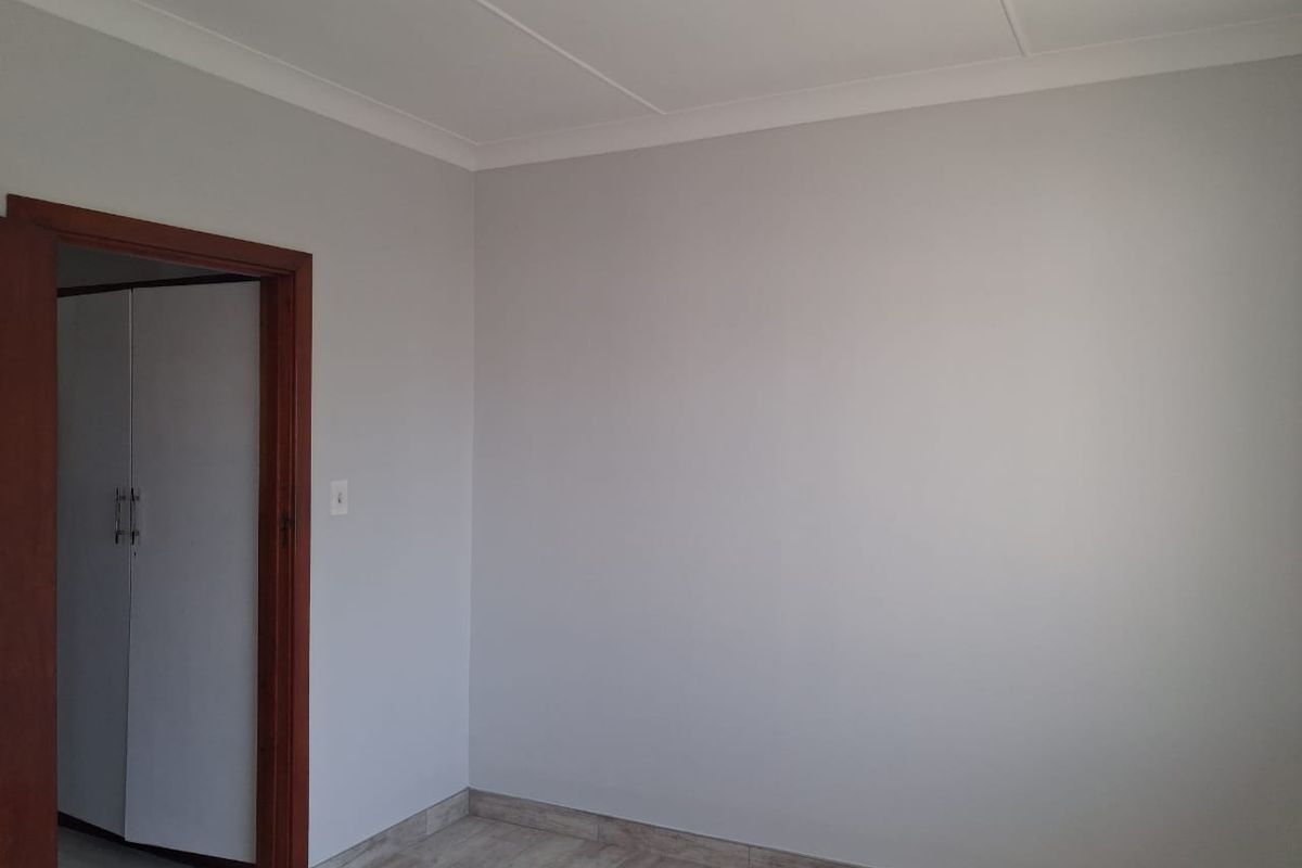 A clean, neutral bedroom featuring tiled flooring, coved ceilings, and a wooden door frame leading to a built-in cupboard area.