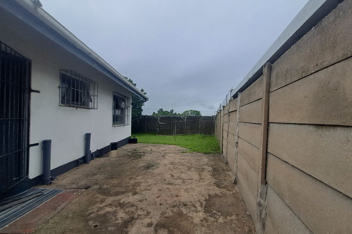 A rear exterior view showing a concrete paved area, precast boundary wall, and security bars on the windows of the main dwelling.