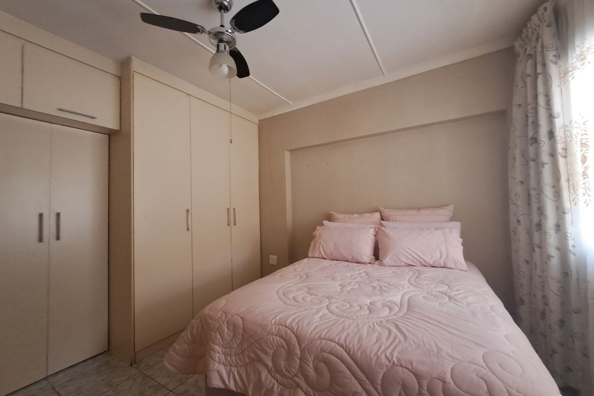 A bedroom featuring built-in cupboards, a ceiling fan, and tiled flooring, offering a functional and neutral space.