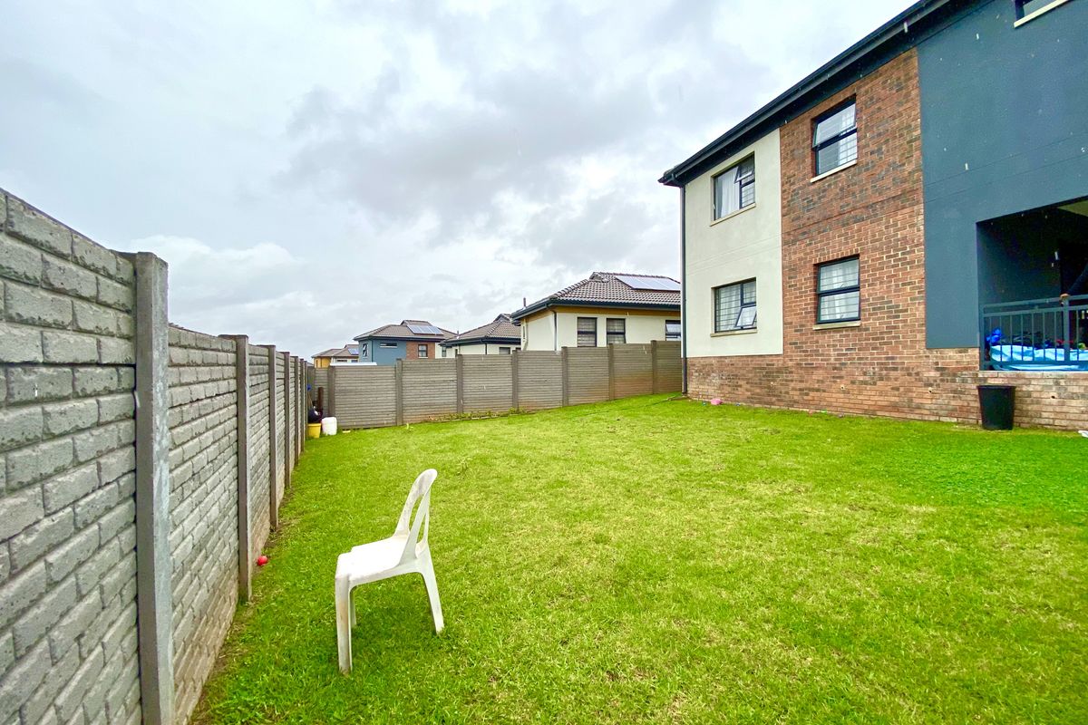 A private rear garden featuring a well-maintained lawn, enclosed by precast concrete boundary walls, adjacent to the brick and plaster exterior of the house.