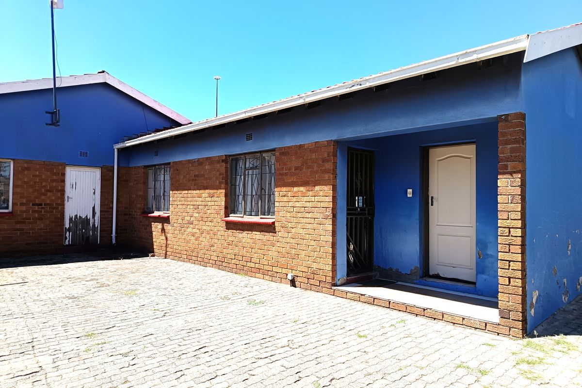 Rear exterior view of the property featuring a paved courtyard, brick and painted facade, and secure entrance doors.