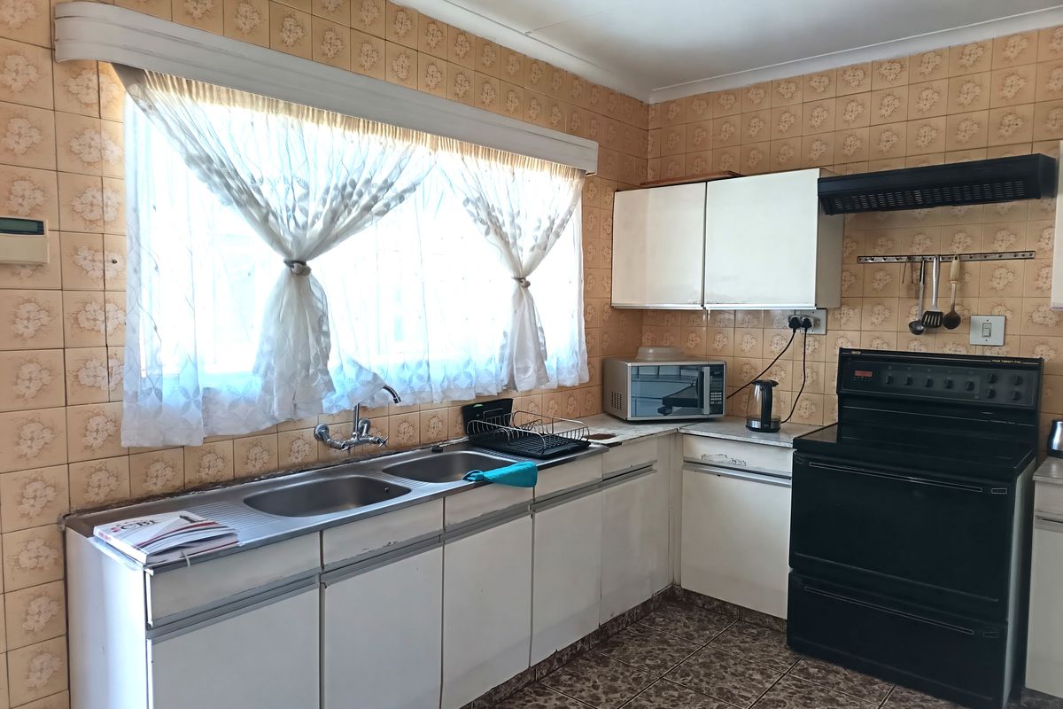 A functional kitchen featuring dated wall tiles, built-in cabinetry, a double basin sink, and a freestanding stove with an extractor fan.