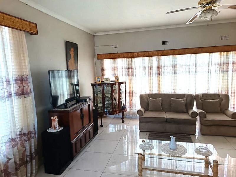 A spacious living room featuring polished tiled flooring, ceiling fan, and large windows with natural light, offering a comfortable and functional living space.