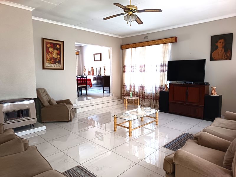 Spacious living room featuring polished tiled flooring, a built-in fireplace, and a ceiling fan, with an elevated transition area leading to the dining space.