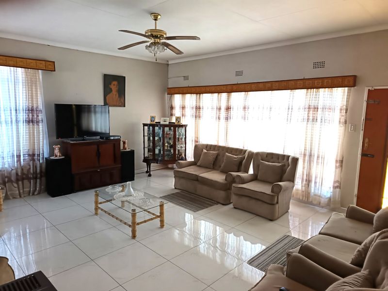 A spacious living room featuring large windows with natural light, tiled flooring, and a ceiling fan, offering a comfortable and bright living area.