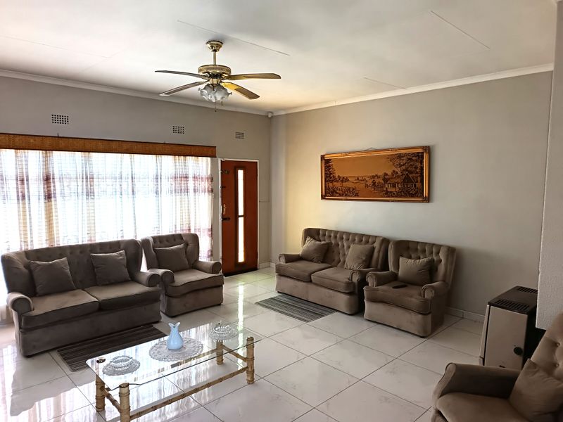 A spacious living room featuring neutral tiled flooring, a ceiling fan, and large windows that provide ample natural light.