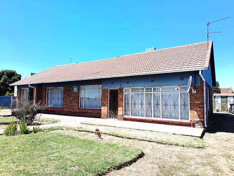 Front view of a single-story brick house featuring a tiled roof, security bars on windows, and a paved entrance area.
