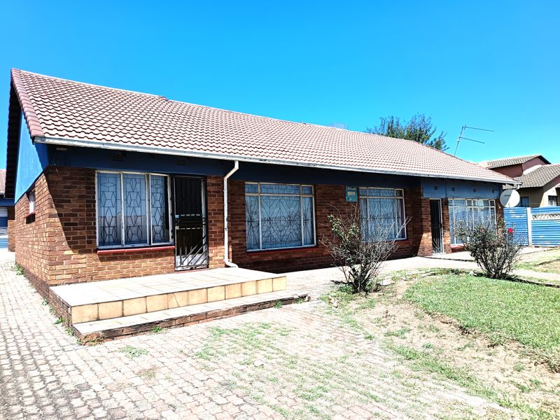Front elevation of a single-story brick house featuring a tiled roof, security gates, and a paved entrance area.