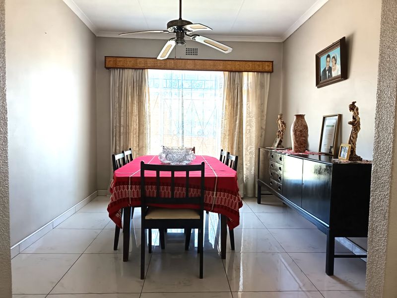 A dining room featuring tiled flooring, a ceiling fan, and a large window with a security gate and decorative pelmet.