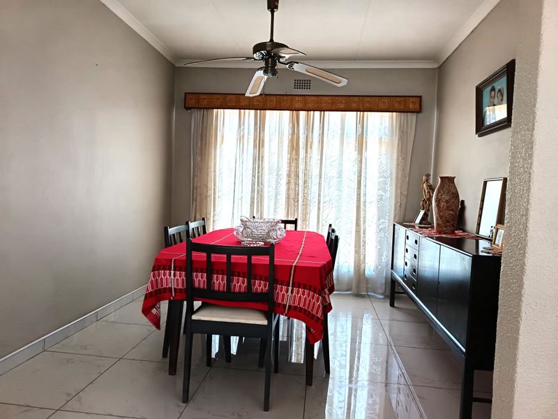 A well-lit dining room featuring polished tiled flooring, a central ceiling fan, and large windows with decorative pelmet detailing.
