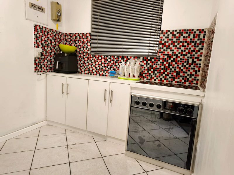 Compact kitchen featuring white cabinetry, a built-in electric stove and oven, and a distinctive red, black, and white mosaic tiled backsplash.
