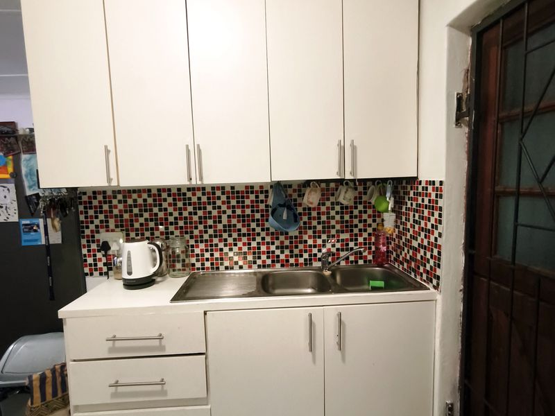 A functional scullery area featuring white cabinetry, a stainless steel sink, and a vibrant mosaic tile backsplash.