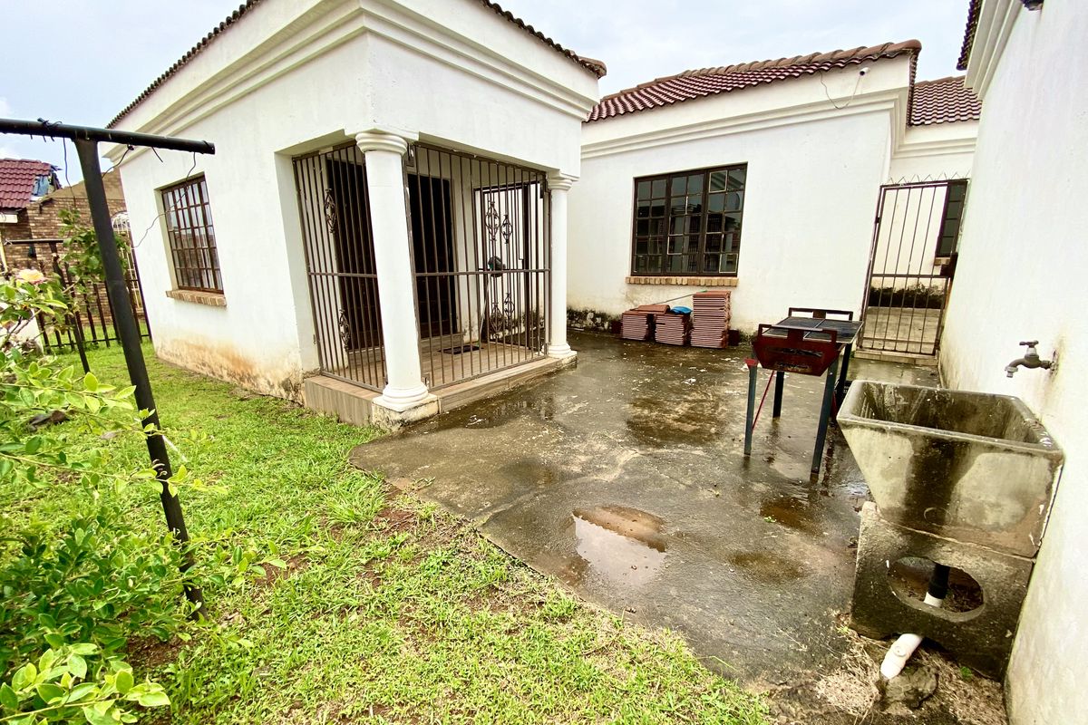 Rear exterior view featuring a concrete patio, security gate, and utility wash basin, showing signs of wear on the building facade and paving.