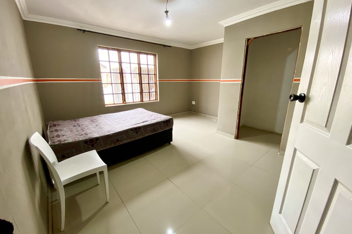 A bedroom featuring tiled flooring, a window with security bars, and a doorway leading to an adjacent space.