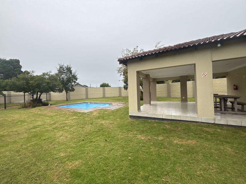 Spacious rear garden featuring a covered patio area, a swimming pool, and a secure perimeter wall, ideal for outdoor entertaining.